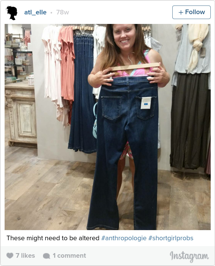 Woman holding oversized jeans, illustrating short people problems with clothing fit issues in a store setting.