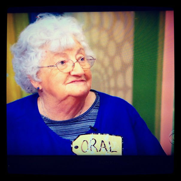 An older woman with glasses wearing a tag labeled with a funny name at a colorful event.