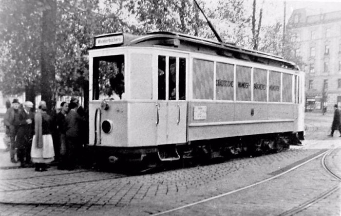 Vintage libraries-on-wheels trolley serving bookmobile patrons in a city setting with people gathered around its entrance.