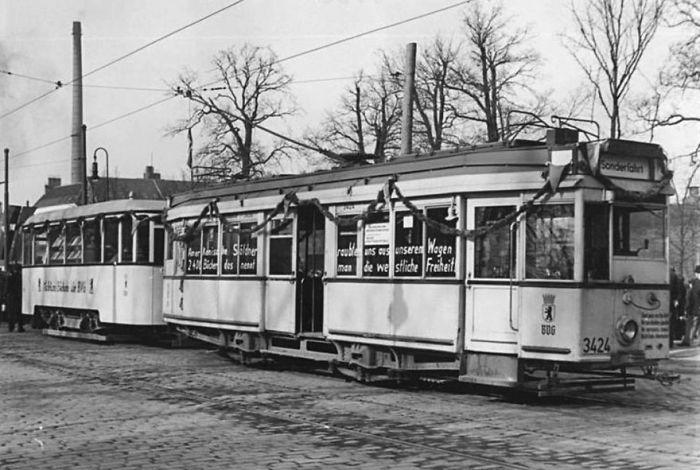 A black and white photo of a historic bookmobile tram parked on a cobblestone street in winter.