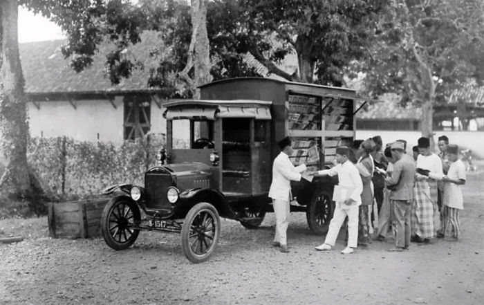 Vintage bookmobile truck with shelves of books serving a group of people outdoors, showcasing libraries-on-wheels history.