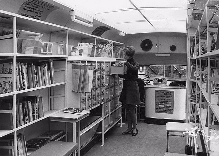 Woman organizing books inside a vintage bookmobile, showcasing a mobile library with shelves and card catalog drawers.