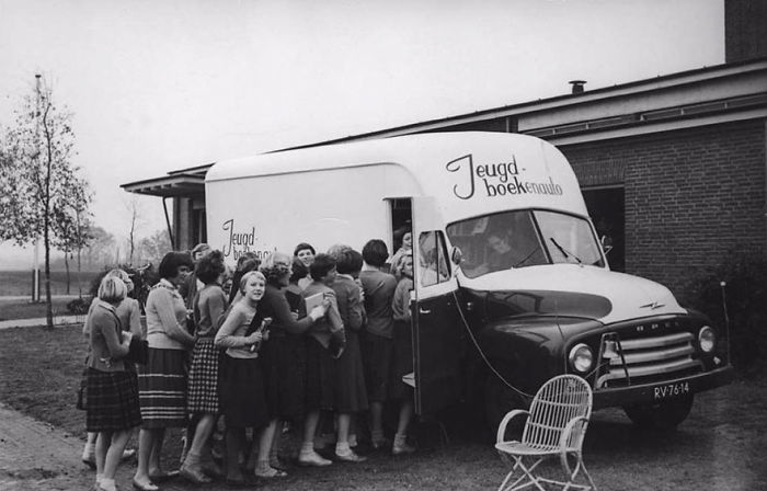Children queuing to borrow books from a vintage bookmobile, an early example of libraries-on-wheels in a community setting.