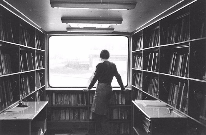 Person standing inside a vintage bookmobile surrounded by shelves filled with books in a mobile library setting.