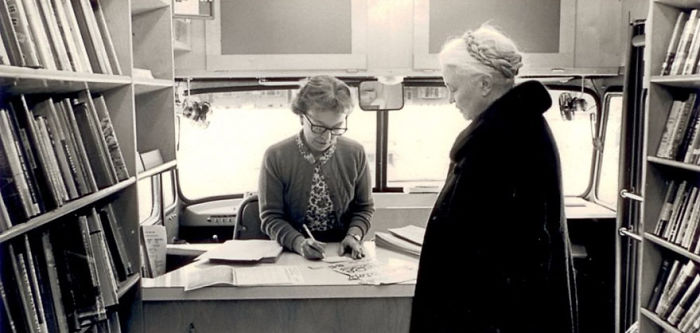 Woman checking out books inside a vintage bookmobile, showcasing libraries-on-wheels and mobile library history.