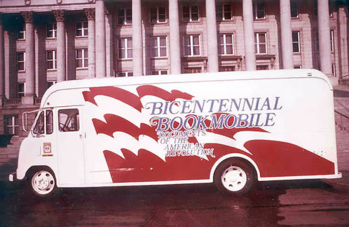 Vintage bicentennial bookmobile vehicle parked in front of a classic government building, showcasing libraries on wheels.