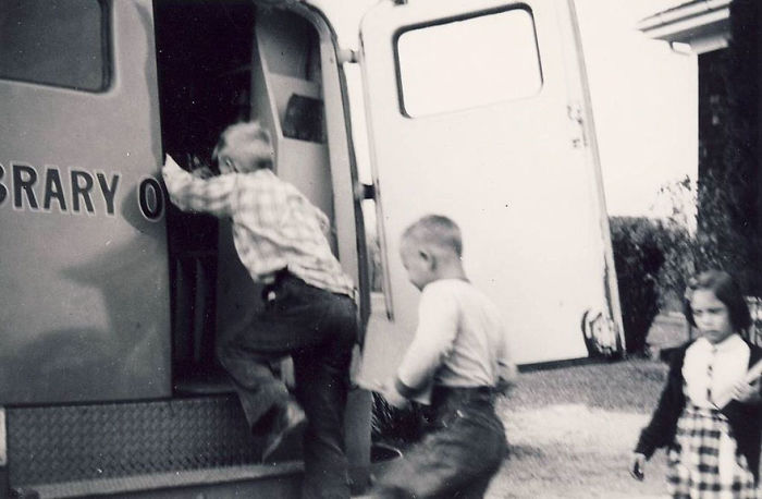 Black and white photo of children entering a bookmobile, an early mobile library vehicle serving local communities.