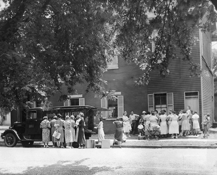 Vintage photo showing a bookmobile parked by a neighborhood with people gathered around libraries-on-wheels.