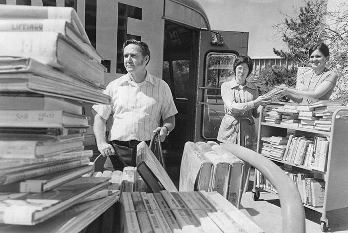 Three people loading books onto a bookmobile, showcasing a rare libraries-on-wheels collection from the past.