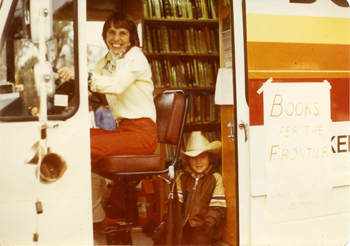 Smiling woman and child inside a vintage bookmobile filled with shelves of books, promoting mobile libraries on wheels.