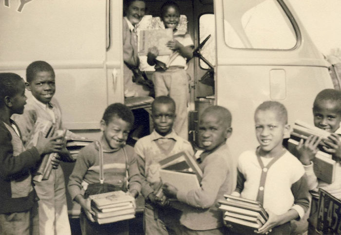 Group of children holding books outside a vintage bookmobile, showcasing rare libraries-on-wheels from the past.