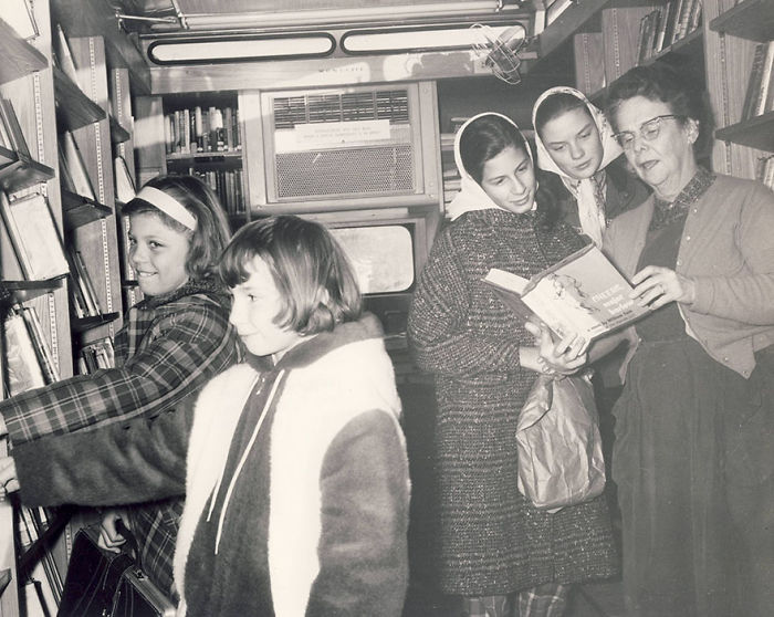 Children and a librarian inside a vintage bookmobile choosing and reading books from library shelves on wheels