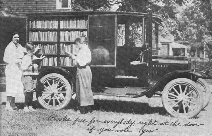 Black and white photo of a vintage bookmobile with bookshelves, children reading, showcasing libraries-on-wheels concept.