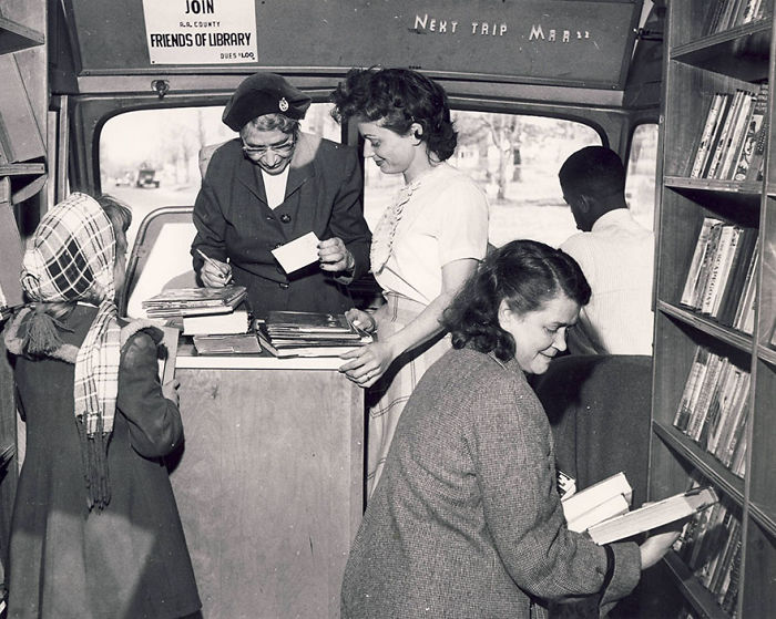 Inside a vintage bookmobile, people browse and check out books from libraries-on-wheels, showcasing mobile library services.