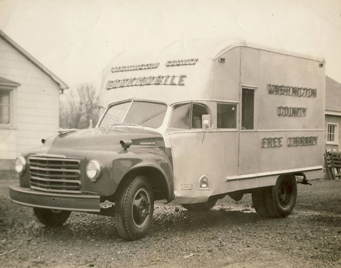 Vintage bookmobile parked outside a house, showcasing libraries-on-wheels as early mobile library services.