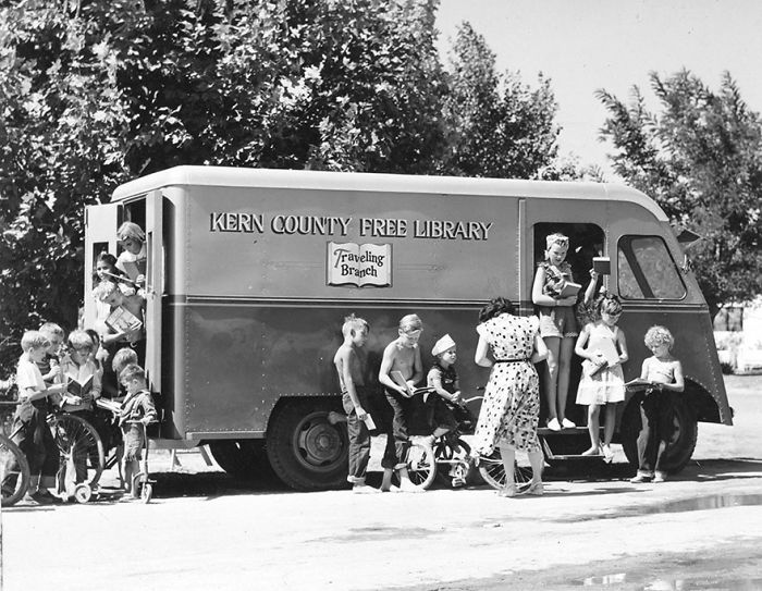 Children gather around a Kern County bookmobile from the traveling branch of the free library on a sunny day.