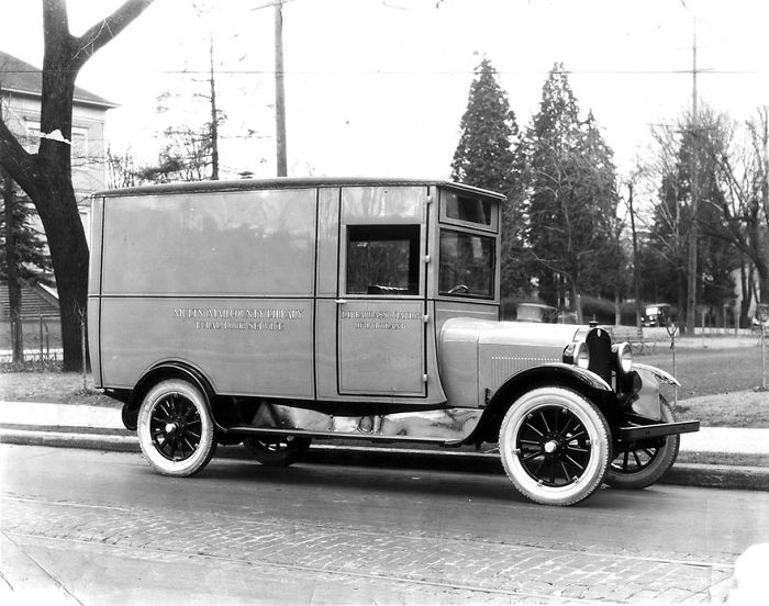 Vintage bookmobile parked on a street, serving as a mobile library in an early 20th century neighborhood.