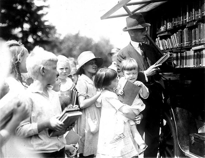 Children and a man selecting books from a vintage bookmobile, showcasing mobile library services before Amazon.