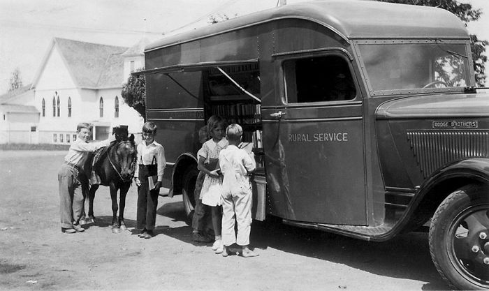 Children browsing books at a vintage bookmobile parked outside near a rural church, showcasing libraries on wheels history.
