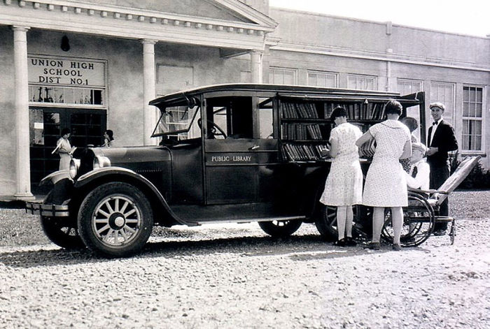 Vintage bookmobile parked outside Union High School with people browsing books from the library-on-wheels in black and white.