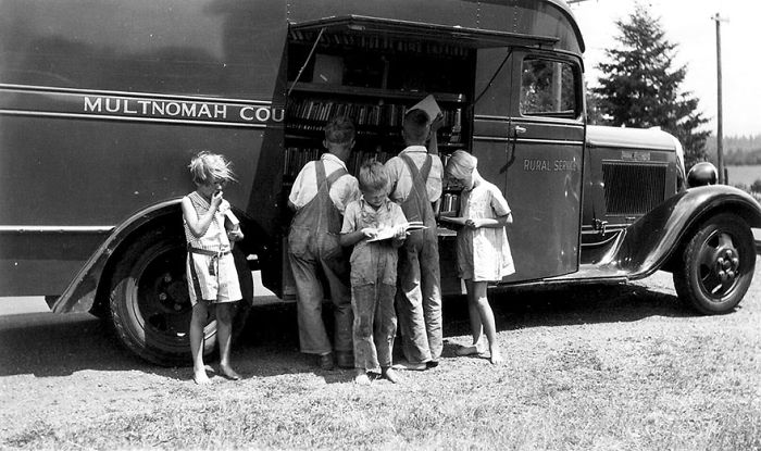 Children gathered around a vintage bookmobile from Multnomah County, exploring books in a rural library-on-wheels setting.