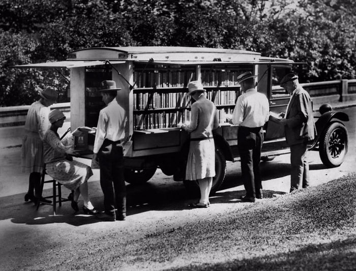 People browsing books at a vintage bookmobile, an early mobile library providing access to books on wheels.