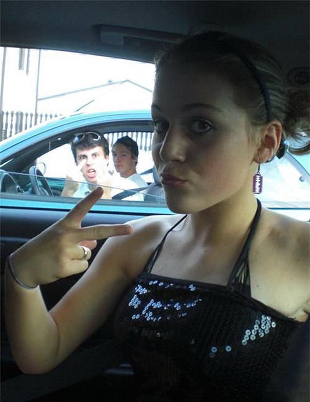 Woman taking a selfie with the man showing middle finger on the background 