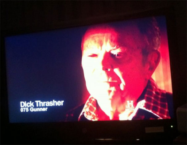 Man with funny name on TV screen labeled "D**k Thrasher," wearing a checkered shirt under red lighting.