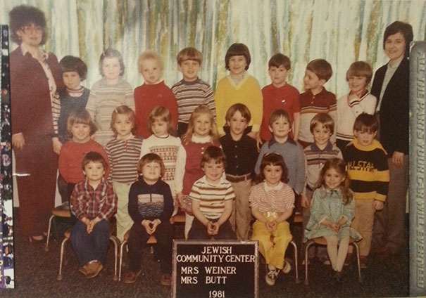 Children in a 1981 class photo with funny teacher names displayed on a sign at a community center.