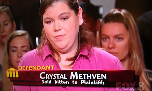 Woman on a TV show with an ironic name, wearing a pink shirt, part of a humorous courtroom scene about kitten sale.