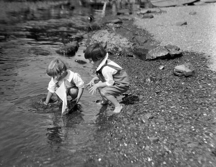 Two Boys Playing At Water's Edge With Toy Sailboat, 1930