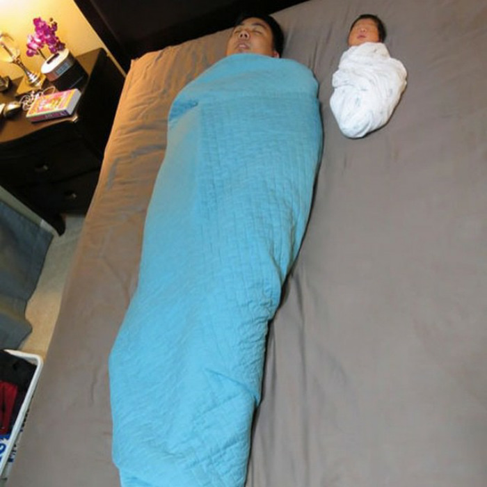 Dad and baby swaddled in blankets on a bed, showcasing a playful dad joke.