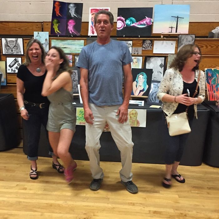 Dad standing humorously in front of an art display with laughing bystanders, showcasing dad jokes.