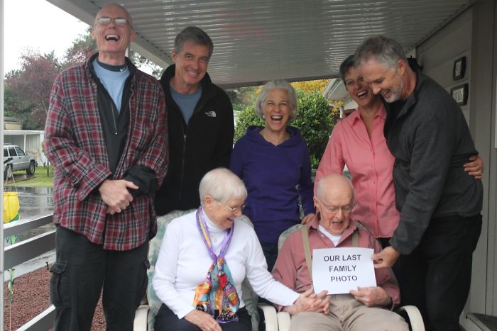 Family laughing as dad holds a humorous "Our Last Family Photo" sign, showcasing dad jokes at another level.