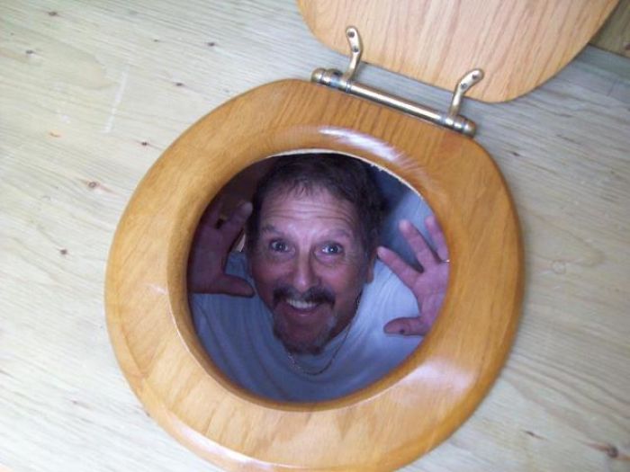 Dad humor at its best: man playfully peering through a toilet seat with a big grin.