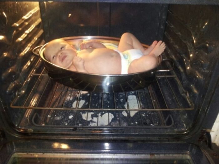 Baby lying in a roasting pan inside an oven, showcasing dads' jokes at another level.