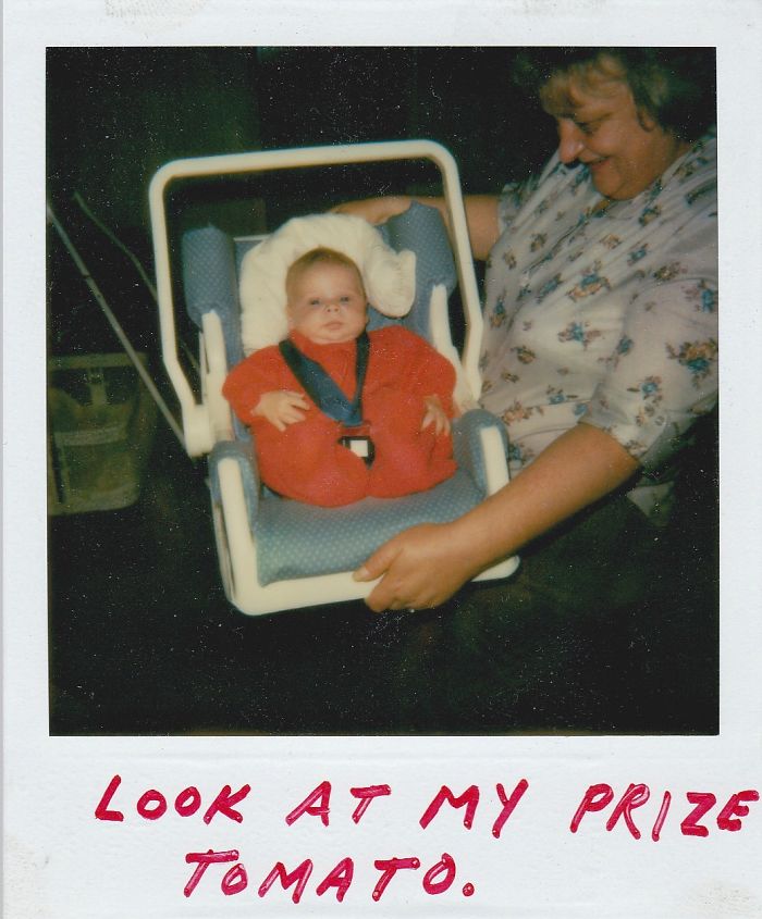 A parent humorously displays a baby in a car seat, dressed as a tomato.