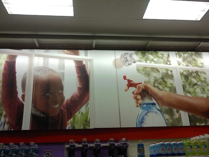 Dad humor: a window cleaner bottle aimed at a photo of a smiling child on a store wall display.