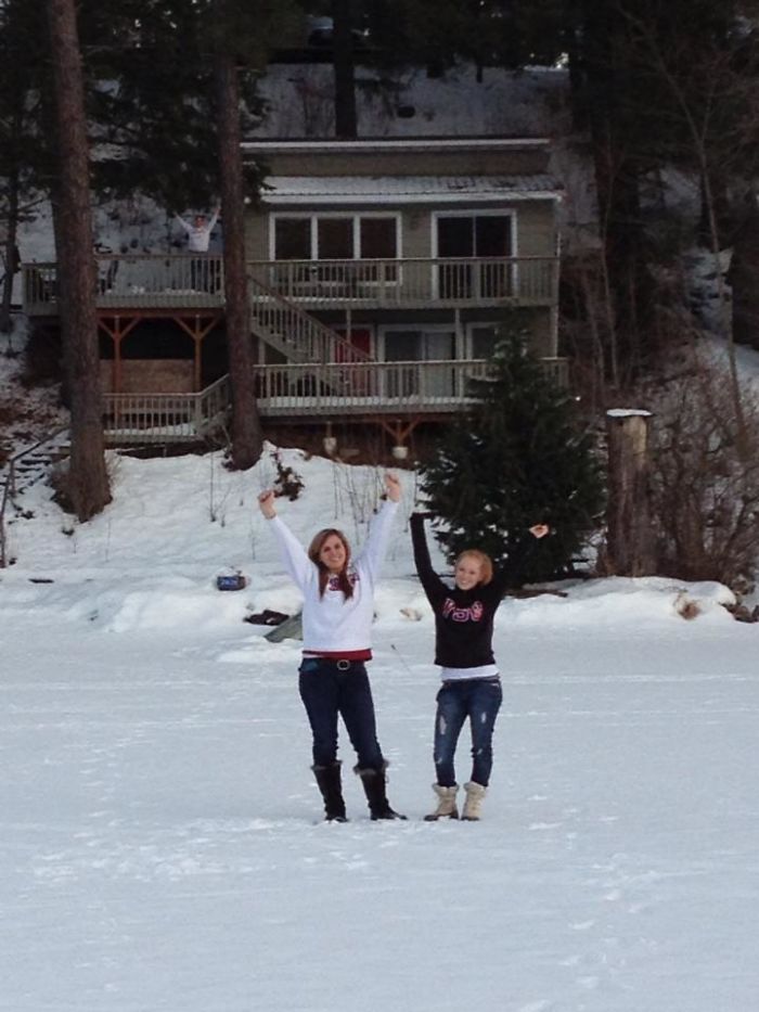 Two girls posing on a snowy field with a dad photobombing from a balcony in the background, showcasing dad jokes.