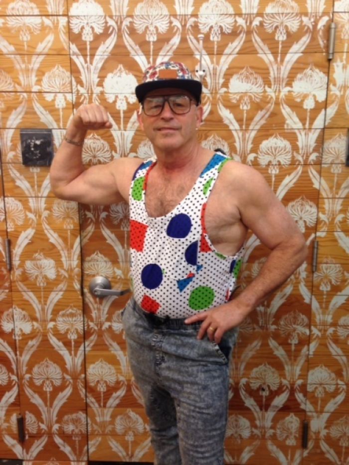 Dad in a colorful outfit, flexing humor with a playful pose, standing against a patterned wallpaper background.