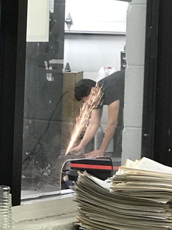 A person using a grinder, sparks flying in a workshop. Stack of papers in the foreground.