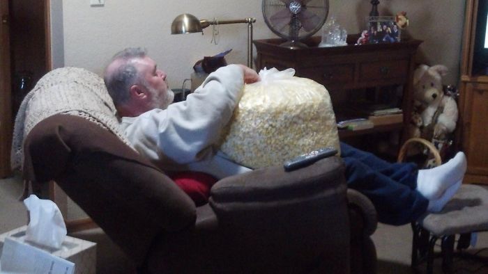 Dad enjoying a huge bag of popcorn in a recliner, illustrating dad jokes at another level.