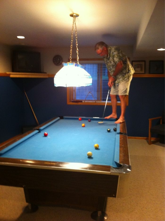 Dad standing on billiard table in a humorous attempt to play pool, showcasing his playful joke.