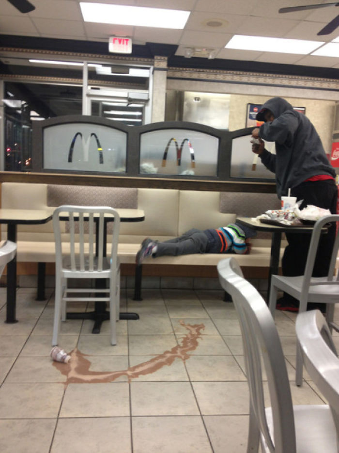 Dad jokingly pretends to capture a disappearing act with spilled drink and child on diner bench.