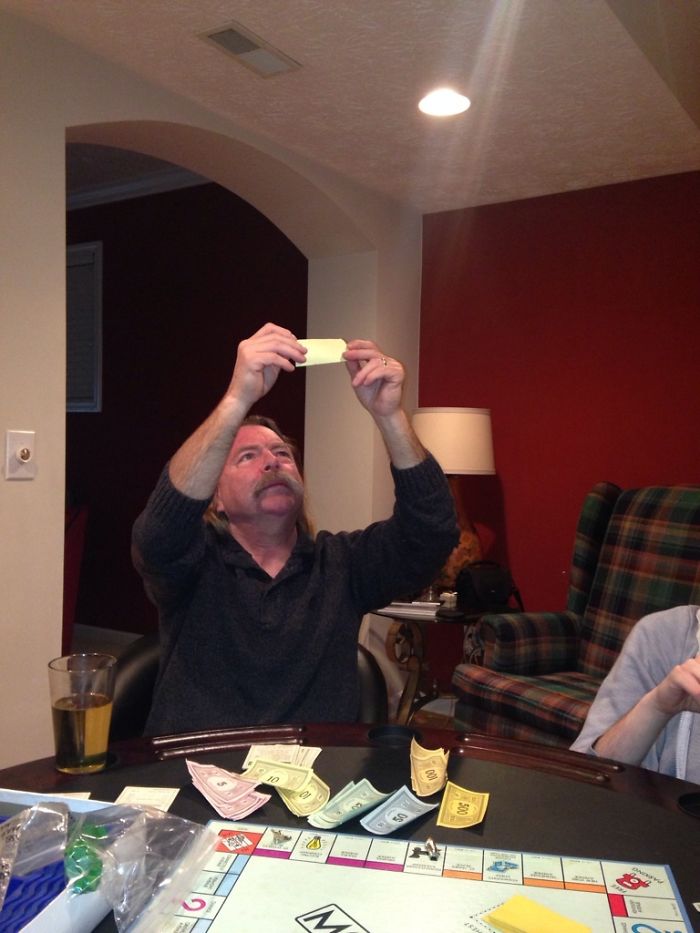 Dad humorously checks Monopoly money under the light during a game night, illustrating classic dad jokes.