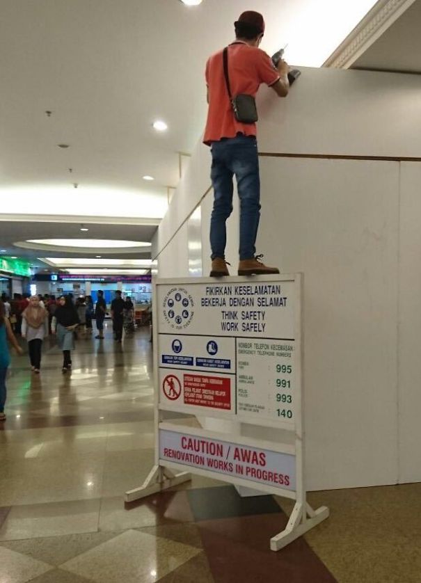 Man standing precariously on a safety sign during renovation, illustrating why women live longer than men.