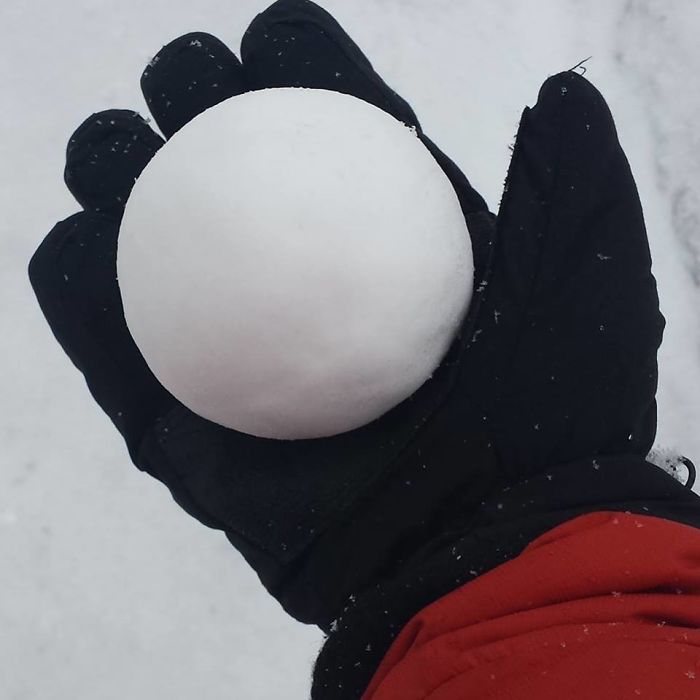 A hand wearing a black glove holds a perfectly round snowball, exemplifying dad jokes taken to another level.