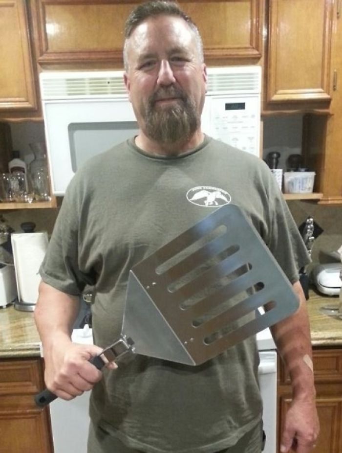 Dad holding oversized spatula, showcasing his sense of humor in the kitchen.