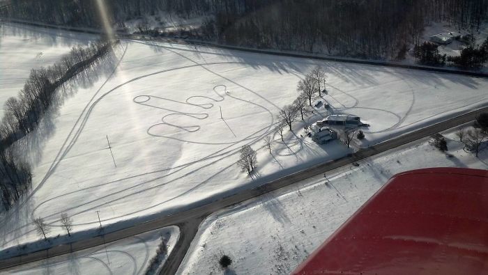 Aerial view of a snow-covered field with a large drawing made by a dad's joke, visible from above.