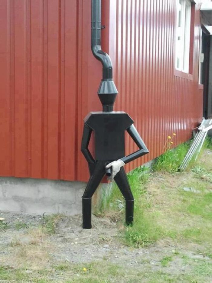 "Creative dad joke sculpture resembling a black pipe figure installed by a red building."